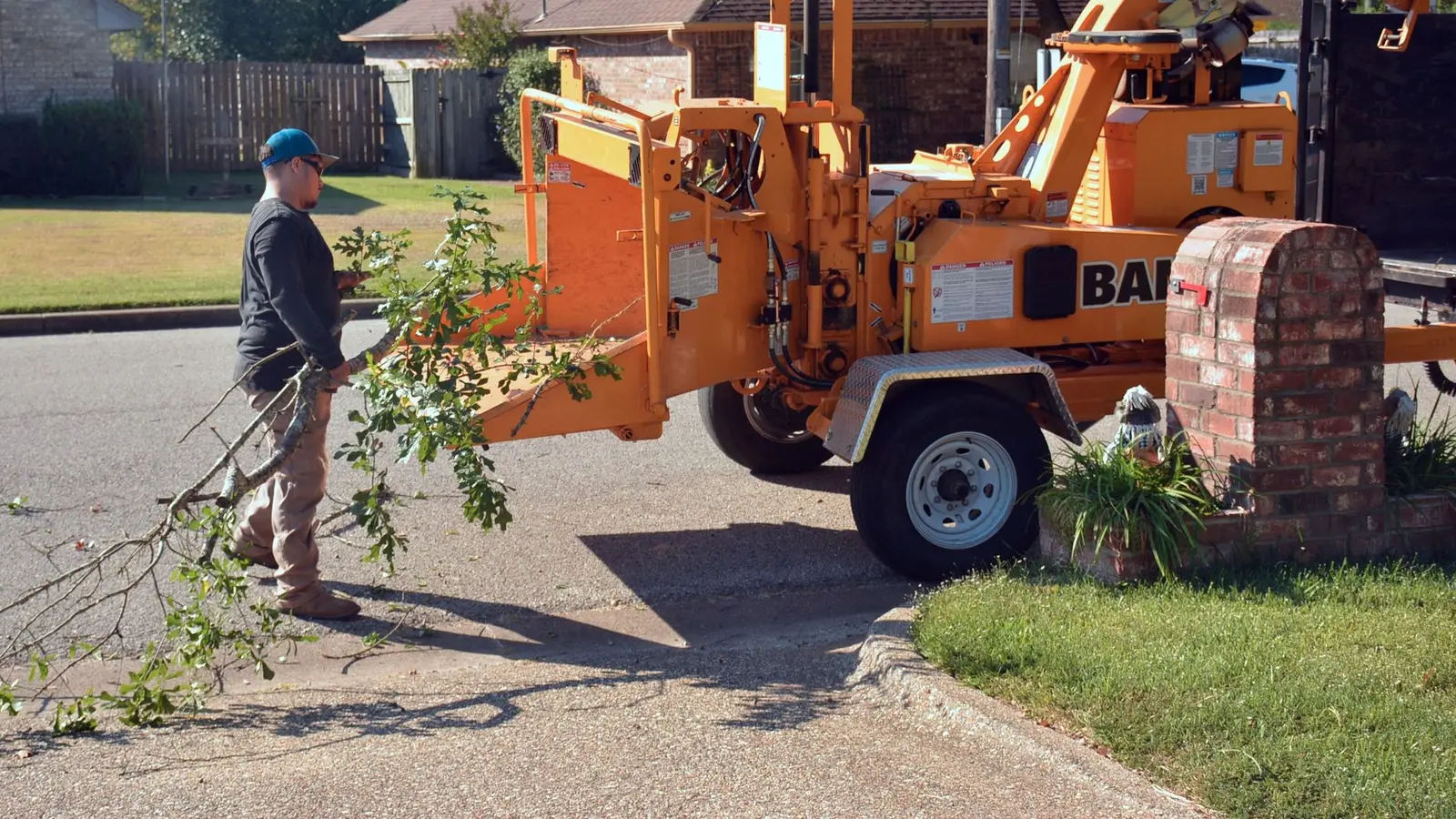 Worker feeding branches into an orange wood chipper parked on a residential street