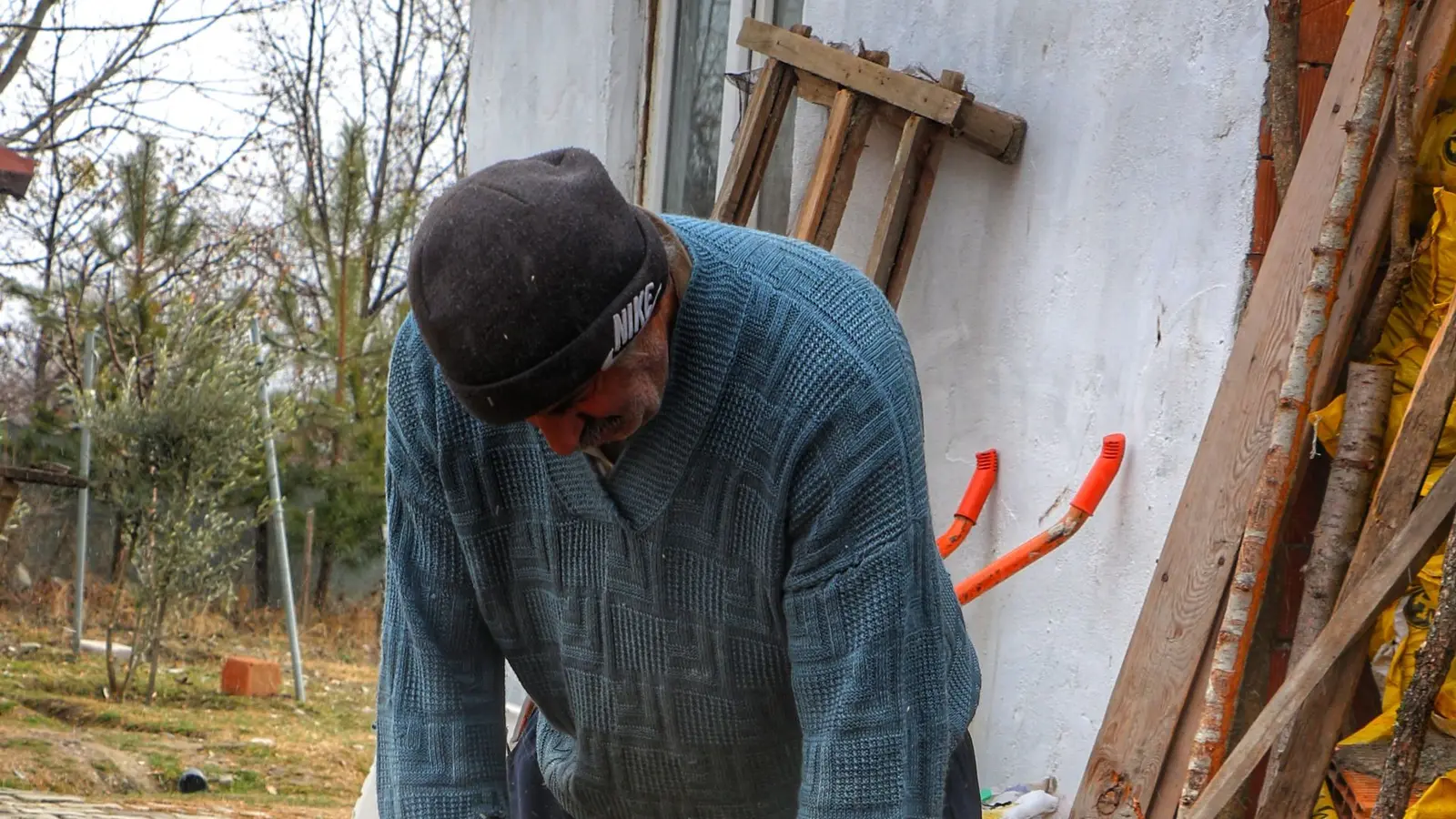 Man cutting a log section with an orange chainsaw beside a wood pile